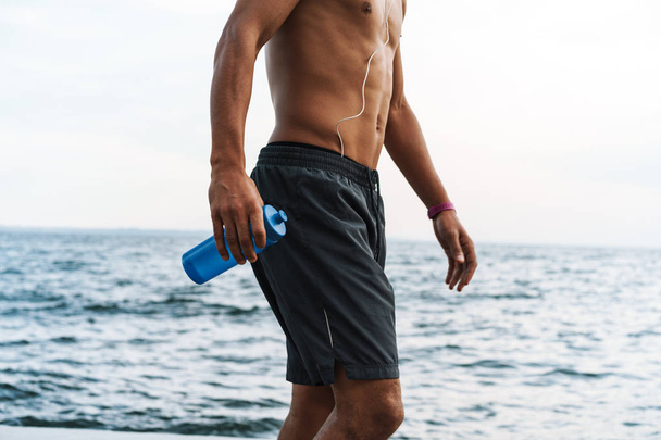 Красивий молодий африканський спортсмен на відкритому повітрі на пляжі морська пляшка з водою
. - Фото, зображення