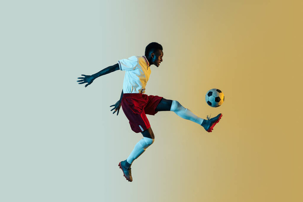 Male soccer player kicking ball in jump isolated on gradient background - Fotoğraf, Görsel