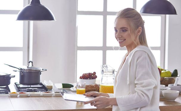 όμορφη νεαρή γυναίκα χρησιμοποιώντας ένα ψηφιακό tablet στην κουζίνα - Φωτογραφία, εικόνα