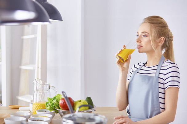 Дівчина за столом на кухні зі склянкою апельсинового джуї
 - Фото, зображення