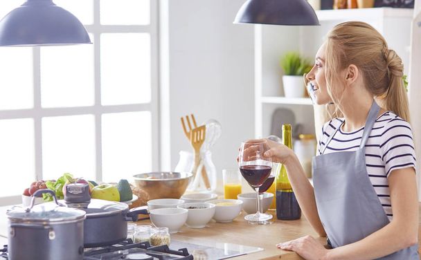 Beautiful woman in kitchen is drinking red wine - Foto, afbeelding