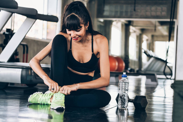 Young happy Caucasian sporty woman tying shoelace on green shoes in gym - Fotó, kép