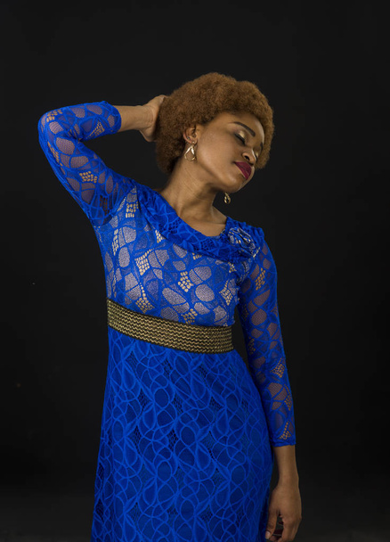 Lady in dress made out of lace. African females beauty concept. Woman with african appearance in blue dress looks gorgeous, black background. Lady on relaxed face with makeup and afro hairstyle - Photo, image