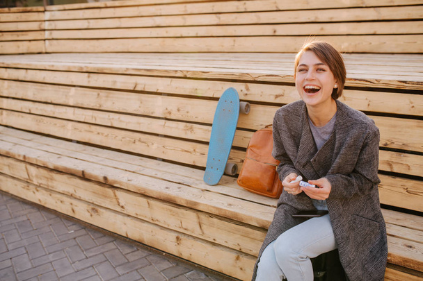 Young laughing woman with a skateboard is sitting on a 2-stage bench. - Fotografie, Obrázek