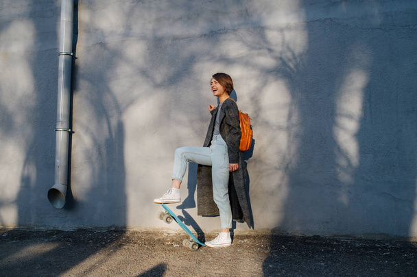 Young happy short-haired brunette woman is taking a stroll with skate in a city. - Photo, image
