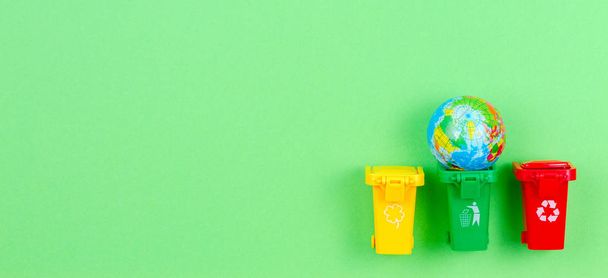 Ecologia problema dell'inquinamento ambientale pianeta, consumismo, concetto di riciclaggio. Mini cestini contenitori con globo su sfondo verde
 - Foto, immagini