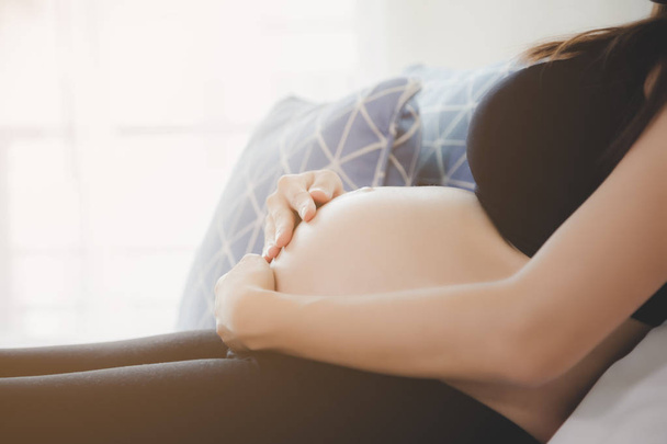 肖像画美しい妊婦。魅力的な美しいママは彼女の腹に触れ、彼女の胎児や赤ちゃんをチェックまたは検査するために医師を待っている間にベッドに座ります。妊娠中の女の子は来月出産します - 写真・画像