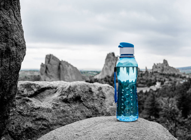 Botella de agua Aqua Blue Fitness sentada sobre roca con montañas en el fondo. Concepto ambiental. Concepto fitness. Concepto de salud
. - Foto, Imagen