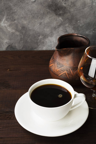 Coffee in white cup with cognac and clay cezve on wooden backgro - 写真・画像