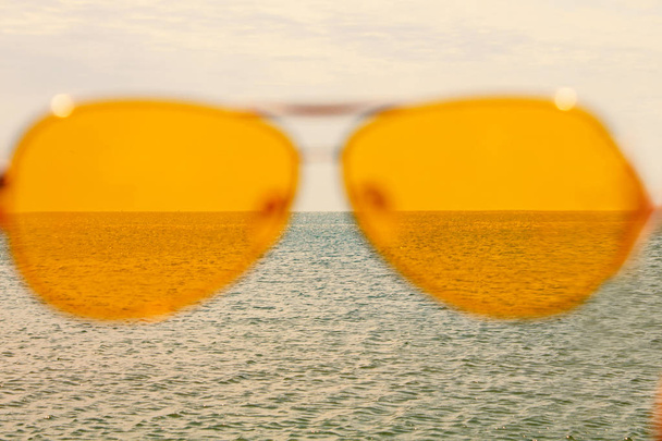 Κίτρινα γυαλιά ηλίου στο θαλασσινό νερό και μπλε φόντο του ουρανού. Καλοκαιρινή ηλιόλουστη μέρα, καλές διακοπές, καλή ξεκούραση, ευτυχία. - Φωτογραφία, εικόνα