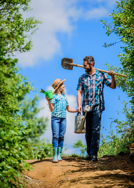 family bonding. spring country side village. father and daughter on rancho. summer farming. farmer man with little girl. garden tools, shovel and watering can. kid worker with dad hold box - Фото, изображение