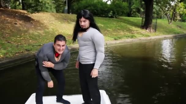 Two attractive men in fake muscle chest and arms padded costumes laugh in boat - Footage, Video