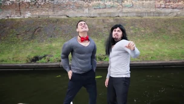 zwei junge Männer in gefälschten muskelgepolsterten Kostümen tanzen und singen im Boot - Filmmaterial, Video