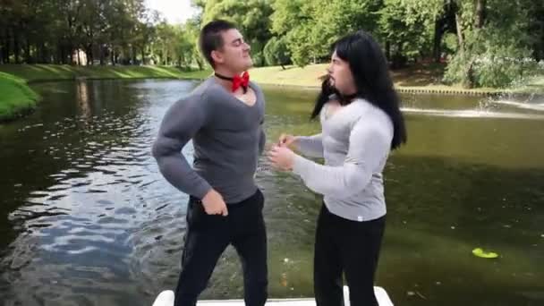 Guys in fake muscle padded costumes tight up bow ties and dance in floating boat - Footage, Video