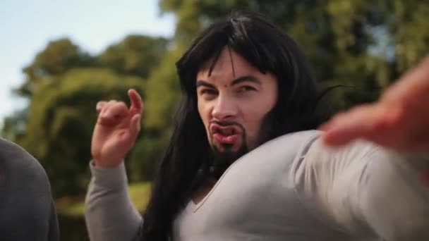Cute young bearded man with long hair and fake muscle costume sings outside. - Footage, Video