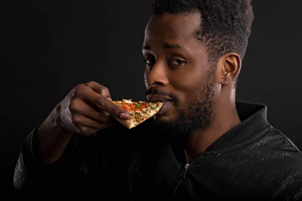 Close up portrait of young african man eating pizza - Fotó, kép
