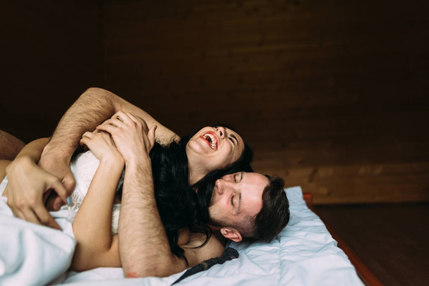 εραστές να κάνουν σεξ στο κρεβάτι στο σπίτι. Ερωτικά παιχνίδια. Ντυμένη σε δαντελωτό εσώρουχο - Φωτογραφία, εικόνα