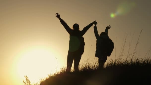 休暇旅行や山で踊るママと娘。夕焼けを見て山の頂上に手を上げた女性。ハイカーガールは手を上げ、勝利を祝い、景色を楽しむ. - 映像、動画