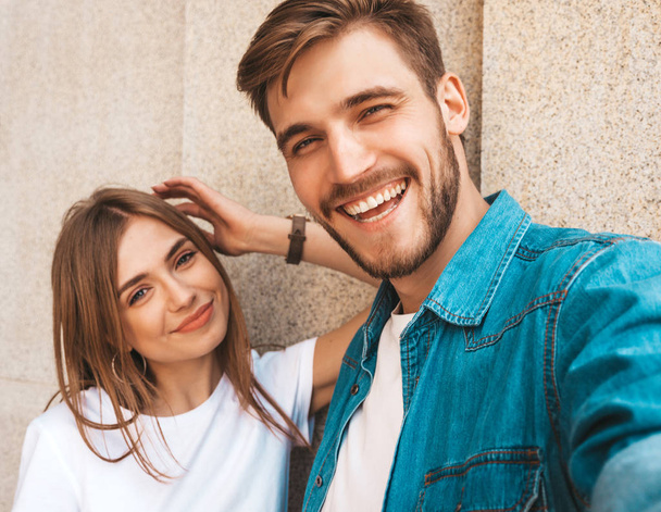 Smiling beautiful girl and her handsome boyfriend in casual summer clothes. Happy family taking selfie self portrait of themselves on smartphone camera. Having fun on the street background  - Foto, Imagem