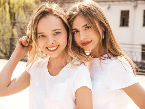 Porträt zweier junger hübscher blonder lächelnder Hipstermädchen in trendiger sommerweißer T-Shirt-Kleidung. sexy unbeschwerte Frauen posieren auf der Straße Hintergrund. Positive Models mit Spaß - Foto, Bild