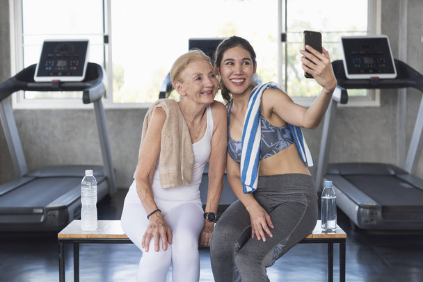 Vrouwen aantrekkelijke glimlachen actieve fitness paar zitten in de sportschool en het nemen van een selfie. - Foto, afbeelding