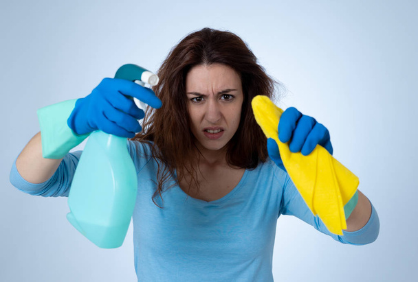Angry and upset woman with cleaning spray and cloth cleaning feeling frustrated. The stain will not come out. In domestic duties and cleaning products advertising image isolated on blue background. - Fotografie, Obrázek