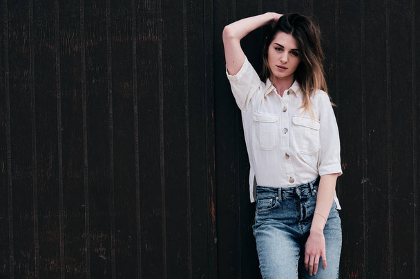 Een jonge hipster mooie vrouw met lang bruin haar in de zomer met denim jeans met een bruine achtergrond - Foto, afbeelding