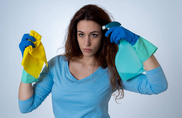 Young beautiful upset housewife woman holding bucket mop cleaning spray feeling stressed tired and frustrated in domestic duties and gender roles concept. Studio shot isolated on blue background. - Fotografie, Obrázek