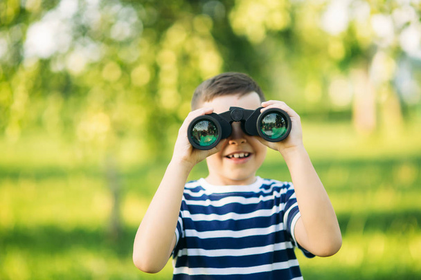 Little boy in a striped t-shirt looks through binoculars .Spring, sunny weather - Photo, image