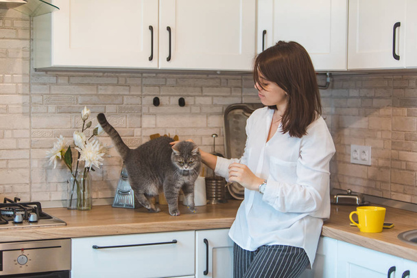 Женщина гладит кошку и пьет чай на кухне
 - Фото, изображение