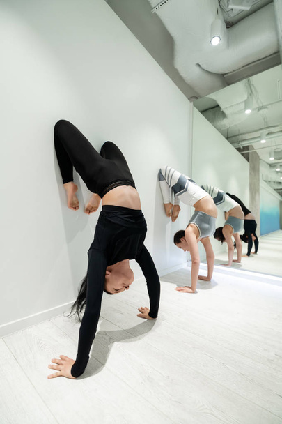 Two fit women loving sport showing amazing yoga poses near wall - Photo, Image