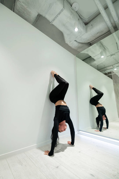 Dark-haired active yoga trainer practicing arm stand near mirror - Фото, зображення