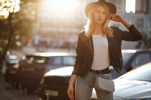 wunderschönes blondes Mädchen mit schwarzem Hut posiert mit warmer Sonne. - Foto, Bild