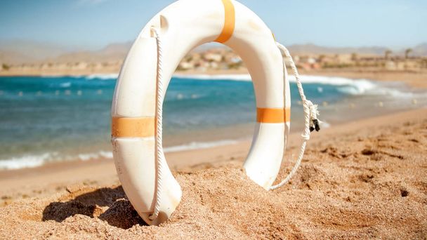 Image rapprochée de l'anneau de sauvetage en plastique blanc sur la plage de la mer par une journée ensoleillée. Plan parfait pour illustrer les vacances d'été à l'océan
. - Photo, image