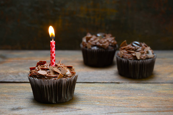Schokoladen-Cupcakes mit brennender Kerze auf rustikalem Holz, dunkelbrauner Hintergrund mit Kopierraum - Foto, Bild