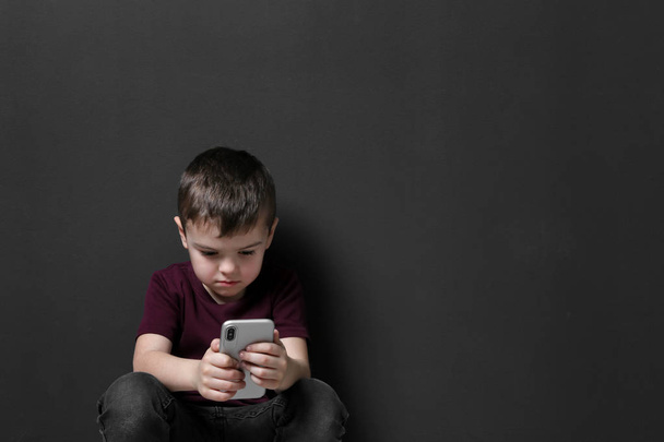 Sad little boy with mobile phone on black background, space for text - Foto, imagen