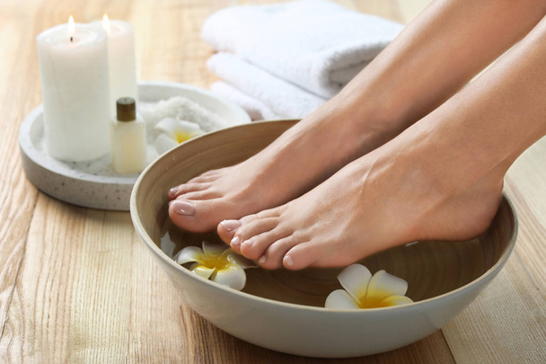 Closeup view of woman soaking her feet in dish with water and flowers on wooden floor. Spa treatment - Foto, imagen