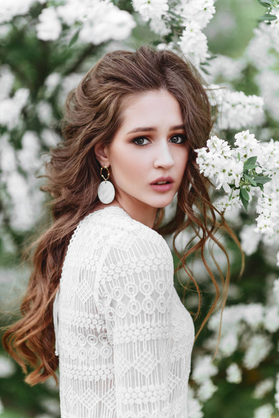 A beautiful young girl stands among the flowering trees. - Foto, afbeelding