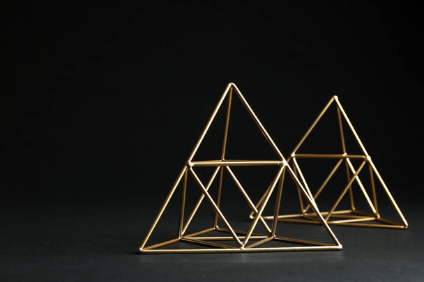 Shiny decorative gold pyramids on black background. Space for text - Foto, Imagem