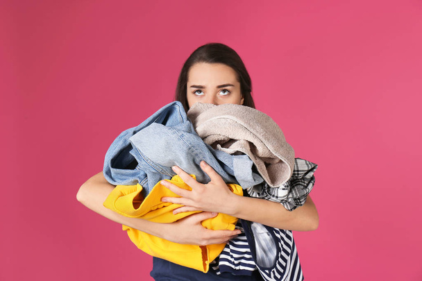 Young woman holding pile of dirty laundry on color background - Valokuva, kuva