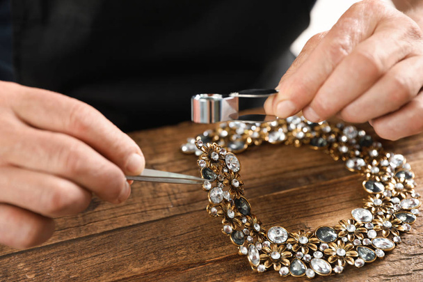 Male jeweler evaluating necklace at table in workshop, closeup - Foto, Imagen