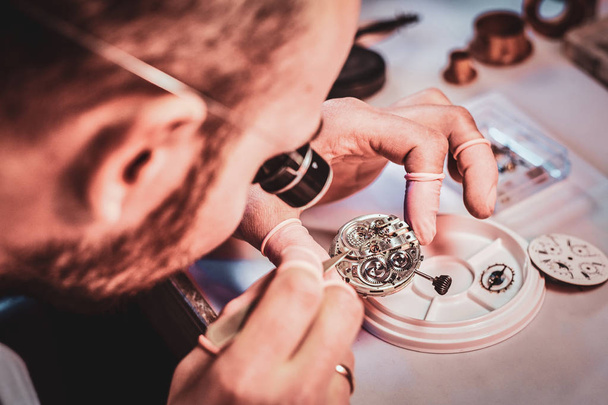 Ώριμη ωρολογιακού Μάστερ διορθώνει παλιά ρολόι για έναν πελάτη στο πολυάσχολο συνεργείο επισκευής του - Φωτογραφία, εικόνα