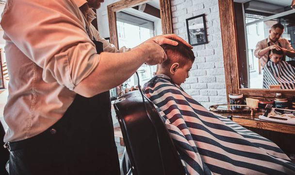 Criança bonito está ficando moderno corte de cabelo de barbeiro na barbearia ocupada
 - Foto, Imagem