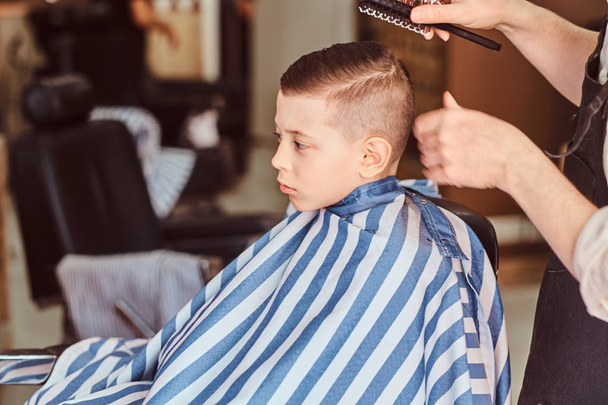 Забавный маленький мальчик стрижется у парикмахера в модном парикмахерском салоне.
 - Фото, изображение