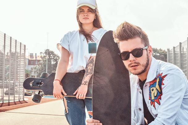 Nuori trendikäs pari on jäähdyttely aurinkoisella kadulla niiden longboards
 - Valokuva, kuva