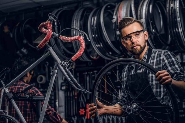 Enfocado hombre atractivo en gafas es chainging rueda para bicicleta en taller ocupado
 - Foto, imagen