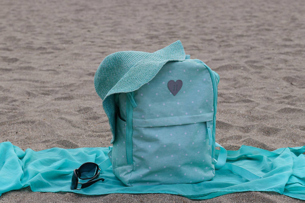 Mochila brilhante, pareo, óculos e chapéu jazem na praia de areia, conceito de viagem de verão, com espaço de cópia para texto
 - Foto, Imagem
