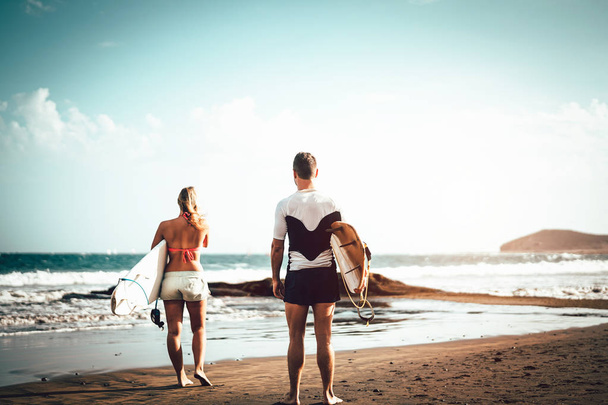 Pár surfařů, kteří stojí na pláži a surfování se chystá surfovat po vysokých vlnách-sportovní mladí lidé se baví během surfování-extrémní sport, vztah a koncept životního stylu mládeže - Fotografie, Obrázek