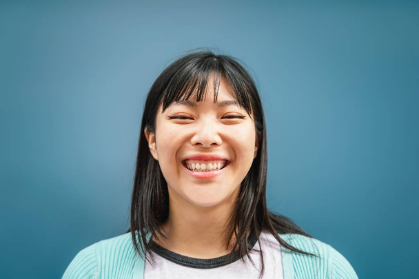 Retrato de una joven asiática sonriendo a la cámara - Mujer china feliz divirtiéndose posando sobre fondo azul - Adolescente, de moda, generación milenaria y estilo de vida de los jóvenes
 - Foto, imagen