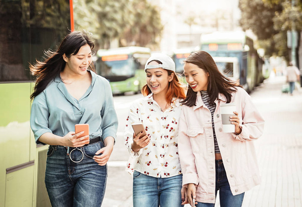 Chicas asiáticas felices usando el teléfono móvil al aire libre - Los jóvenes millennials se divierten con la nueva tecnología de aplicaciones para teléfonos inteligentes - Concepto de amistad, social, tecnología y estilo de vida adolescente
 - Foto, Imagen